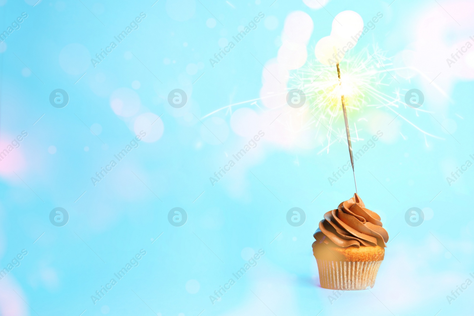 Image of Birthday cupcake with sparkler on light blue background. Space for text