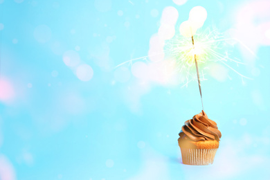 Birthday cupcake with sparkler on light blue background. Space for text