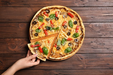 Photo of Woman holding delicious homemade pizza slice on wooden background