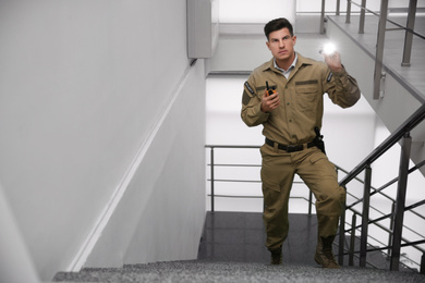 Photo of Professional security guard with portable radio set and flashlight on stairs