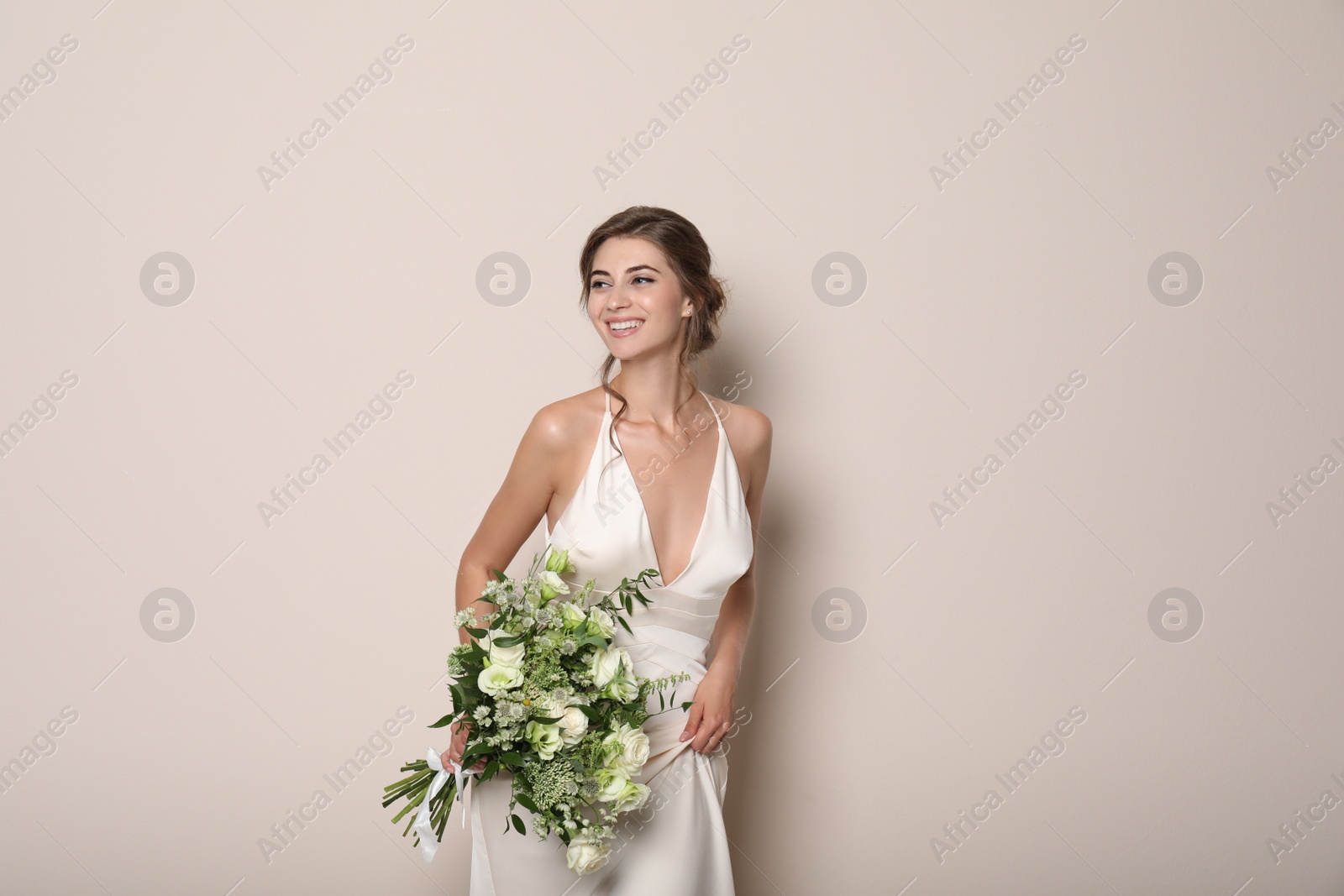 Photo of Young bride wearing wedding dress with beautiful bouquet on beige background