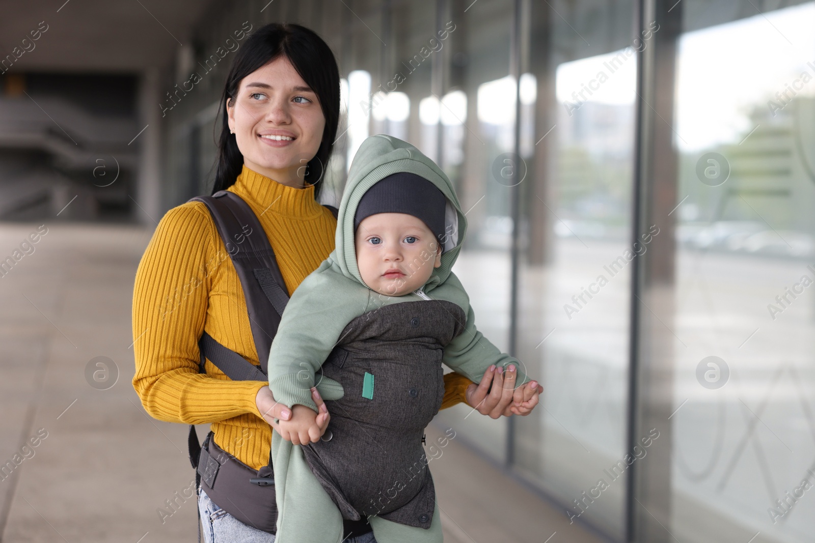 Photo of Mother holding her child in sling (baby carrier) near building outdoors