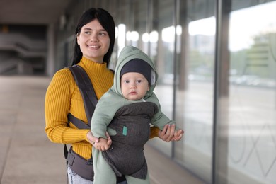 Mother holding her child in sling (baby carrier) near building outdoors