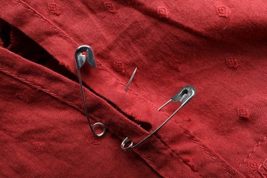 Metal safety pins on red fabric, closeup