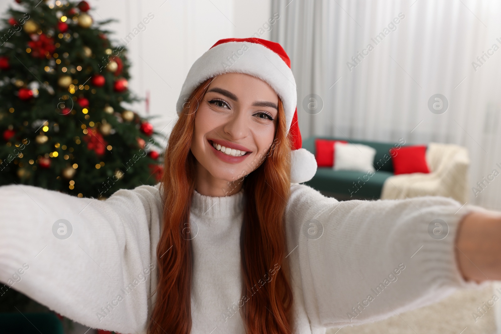 Photo of Beautiful young woman in Santa hat taking selfie at home. Christmas celebration
