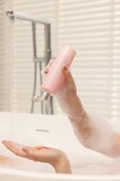 Woman pouring shower gel onto hand in bath indoors, closeup