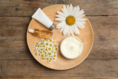 Photo of Composition with chamomile flowers and cosmetic products on wooden table, top view