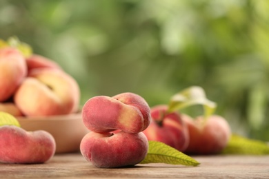 Fresh ripe donut peaches on wooden table against blurred green background. Space for text