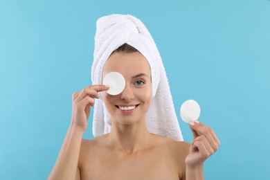 Smiling woman removing makeup with cotton pads on light blue background