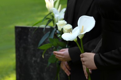 People with flowers outdoors, closeup. Funeral ceremony