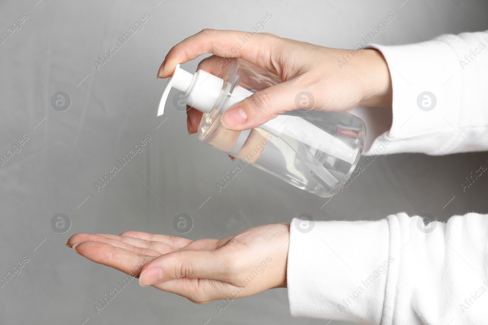 Photo of Woman applying antiseptic gel on hand against light grey background, closeup