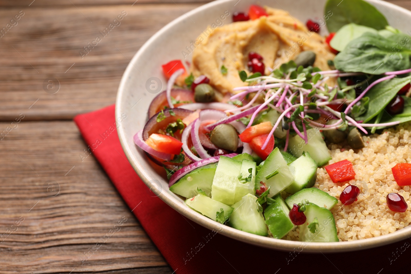 Photo of Delicious vegan bowl with cucumbers, spinach and bulgur on wooden table, closeup
