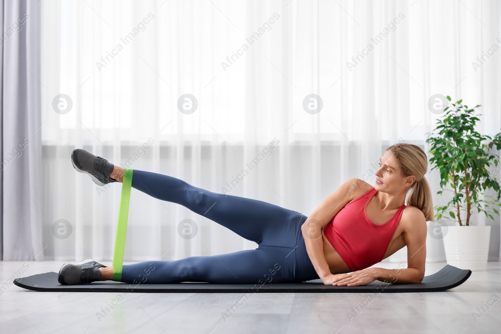 Photo of Athletic woman doing exercise with fitness elastic band on mat at home