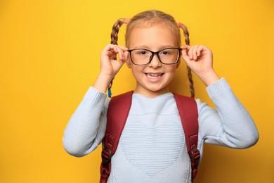 Photo of Cute little girl with backpack wearing glasses on yellow background