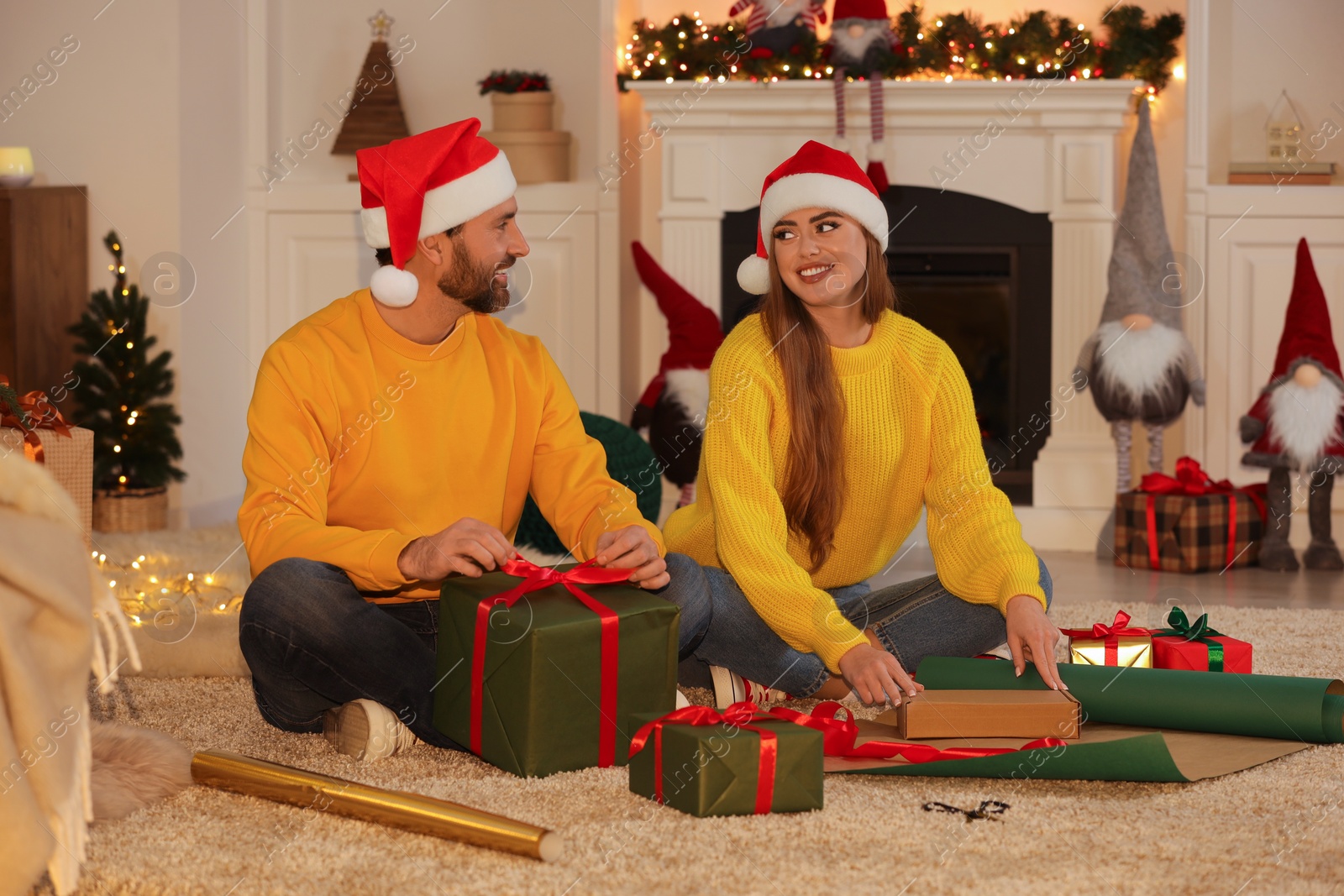 Photo of Happy couple in Santa hats decorating Christmas gifts at home