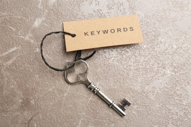 Photo of Vintage key and tag wIth word KEYWORDS on grey table, top view