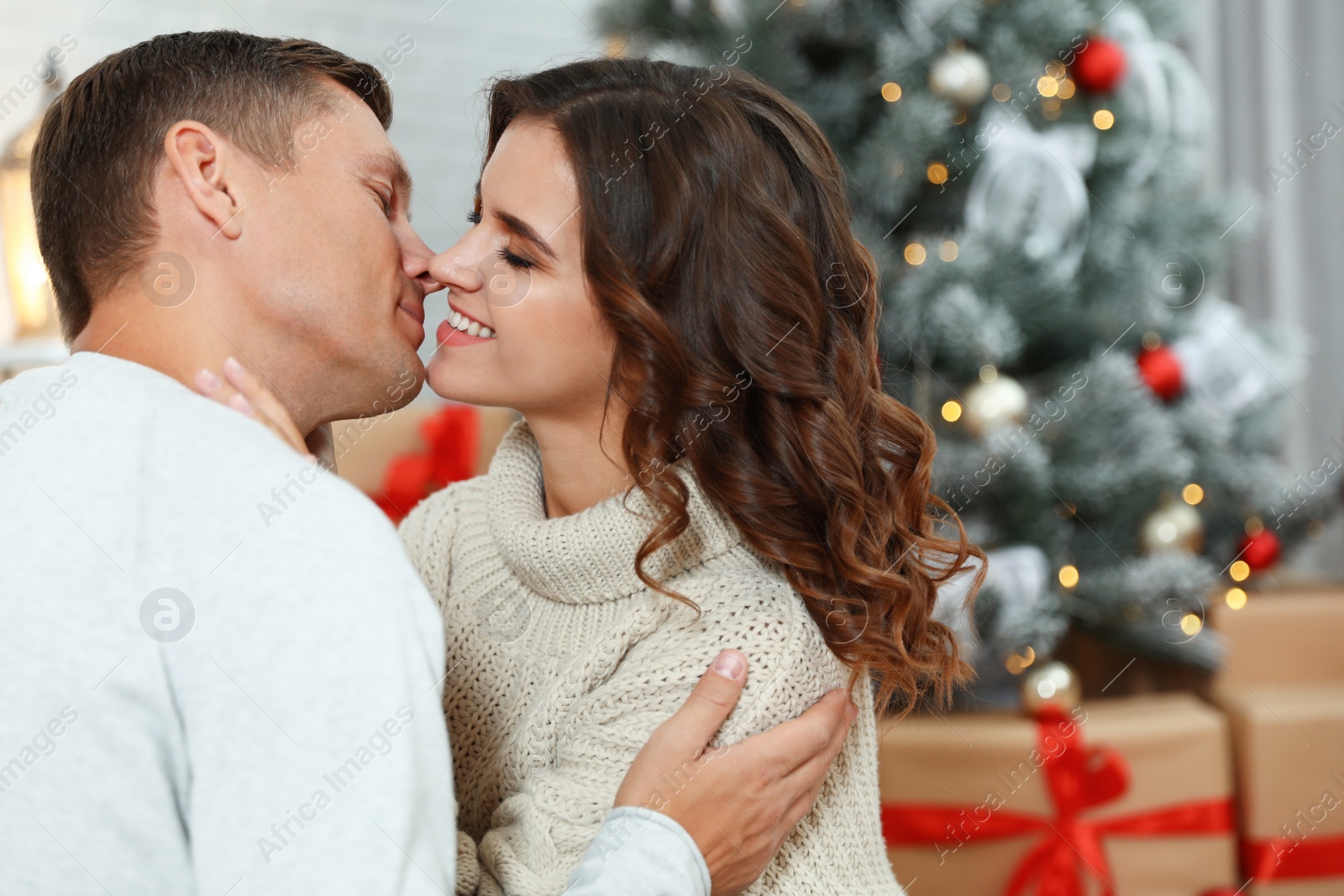 Image of Happy couple kissing near Christmas tree at home