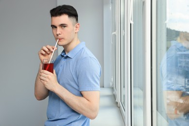 Photo of Handsome young man drinking juice near window at home