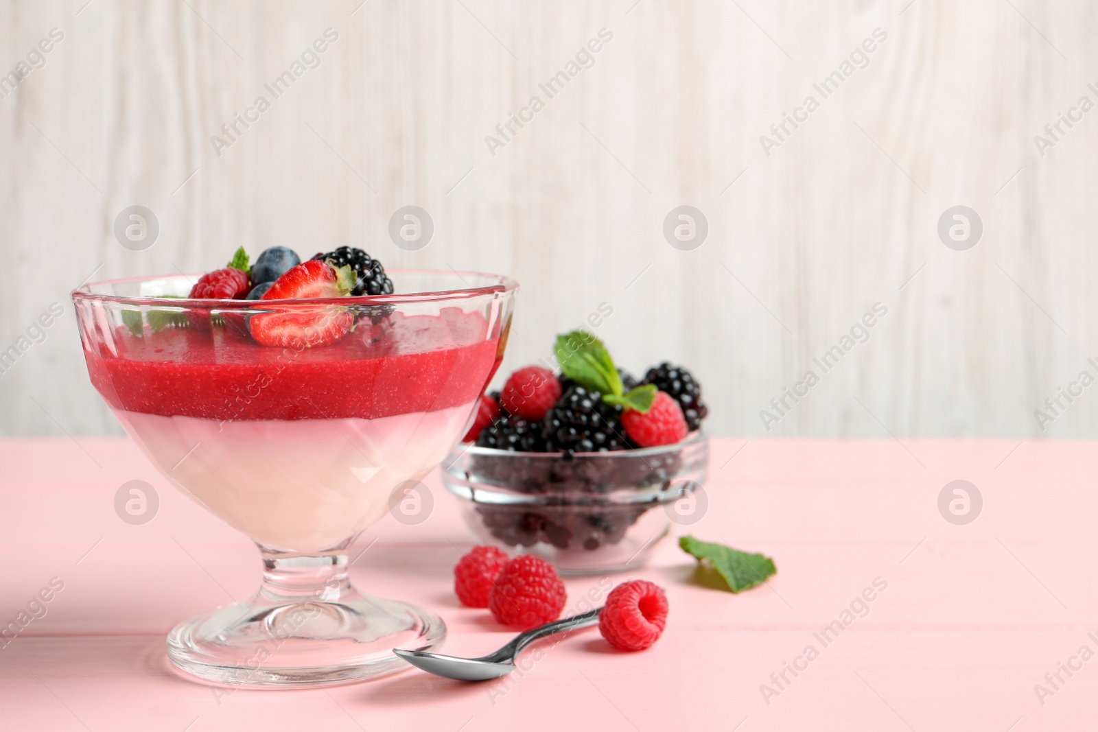 Photo of Delicious panna cotta with fruit coulis and fresh berries served on pink wooden table. Space for text