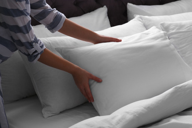 Woman fluffing white pillow on bed, closeup