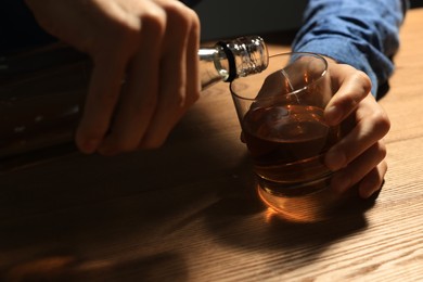 Photo of Addicted man with alcoholic drink at wooden table, closeup