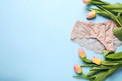 Photo of Elegant beige women's underwear and beautiful tulips on light blue background, flat lay. Space for text