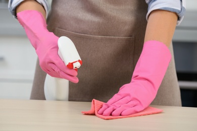 Photo of Woman cleaning table with rag in kitchen, closeup