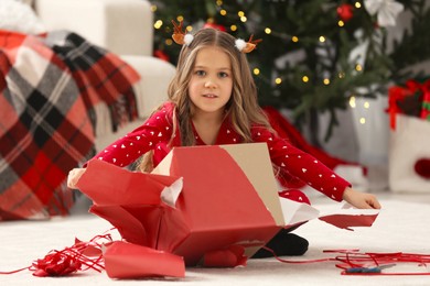 Photo of Cute little girl unwrapping Christmas gift at home