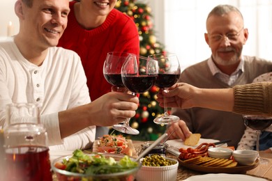Photo of Happy family clinking glasses of wine at festive dinner, focus on hands. Christmas celebration