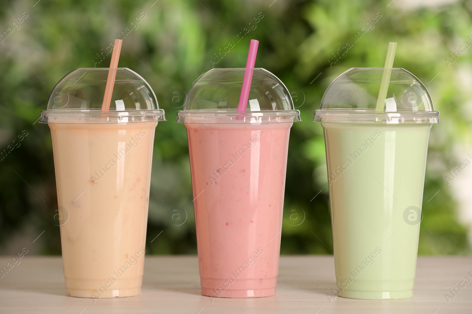 Photo of Plastic cups with different tasty smoothies on wooden table outdoors