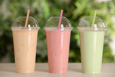 Photo of Plastic cups with different tasty smoothies on wooden table outdoors