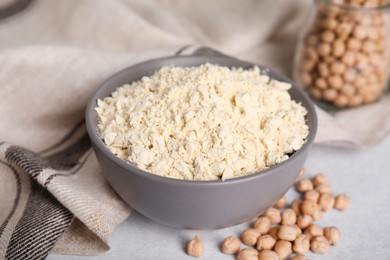 Photo of Chickpea flour in bowl and seeds on light grey table, closeup