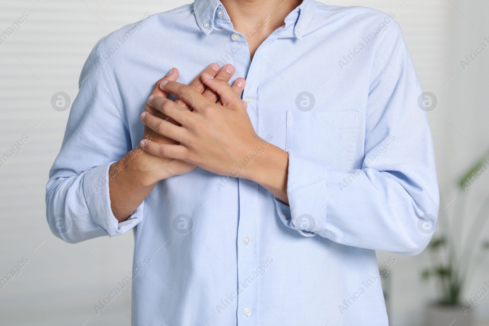 Photo of Thank you gesture. Grateful man with hands on chest indoors, closeup