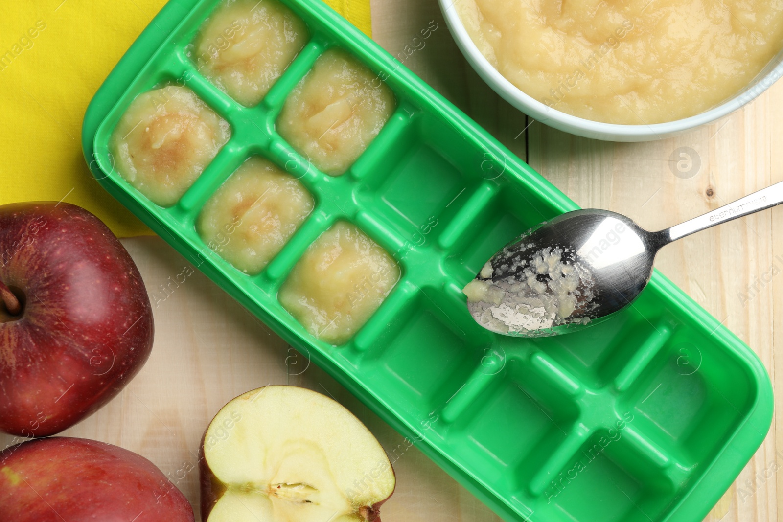 Photo of Apple puree in ice cube tray with fresh apple fruits on wooden table, flat lay. Ready for freezing