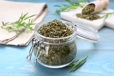 Photo of Jar of dry tarragon and green leaves on light blue wooden table, closeup