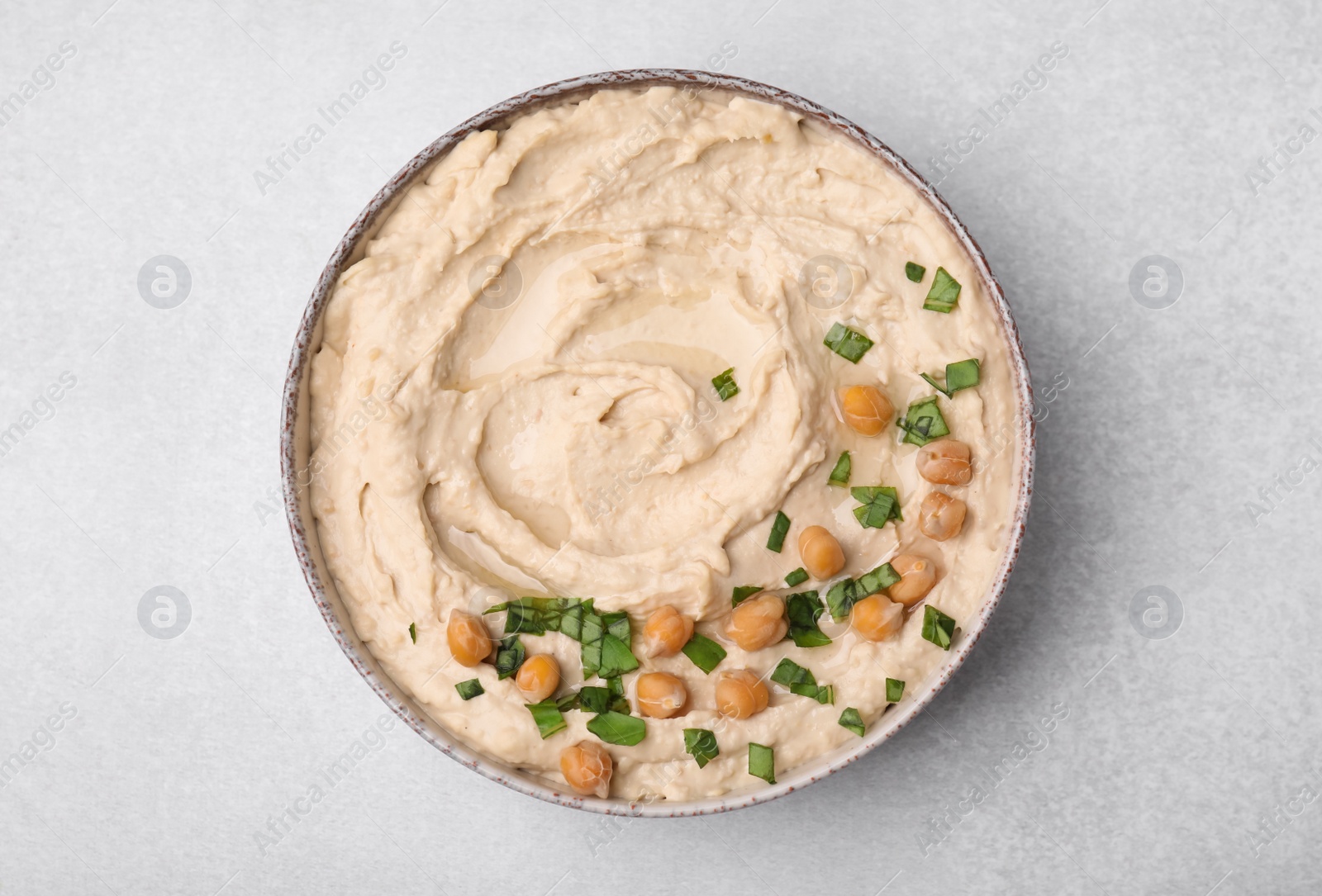 Photo of Bowl of delicious hummus with chickpeas on light grey table, top view