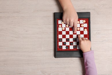 Photo of Children playing checkers at light wooden table, top view. Space for text
