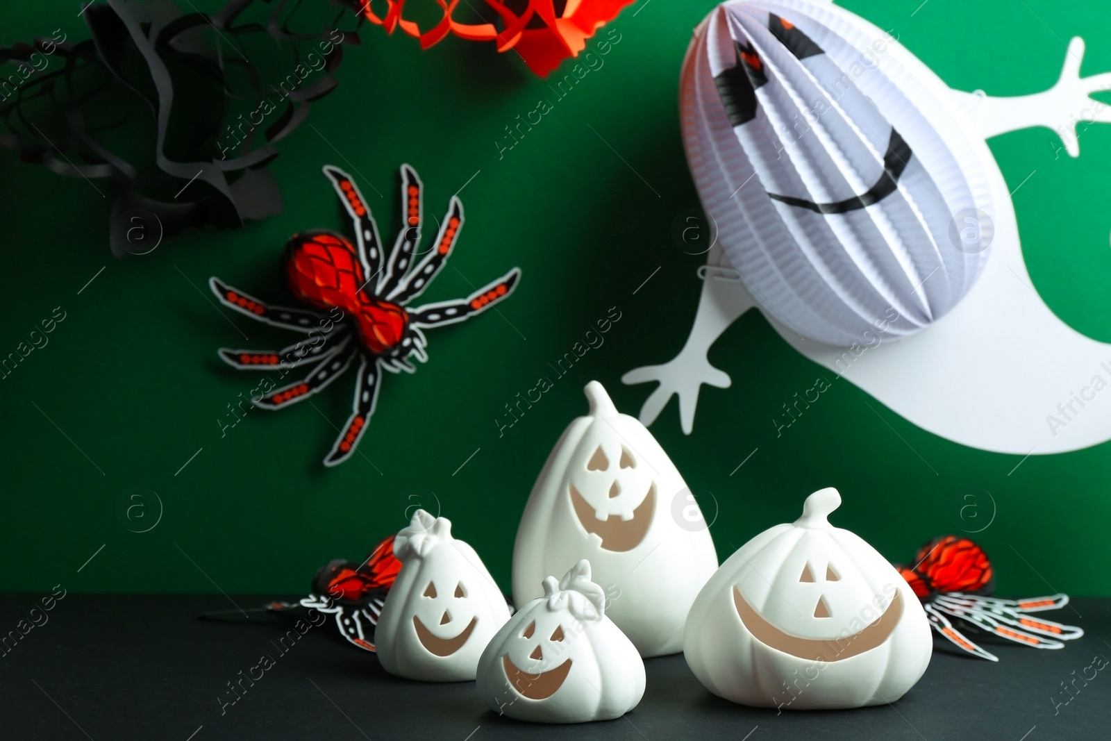 Photo of Composition with pumpkin shaped candle holders on black table against green background. Halloween decoration