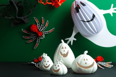 Composition with pumpkin shaped candle holders on black table against green background. Halloween decoration