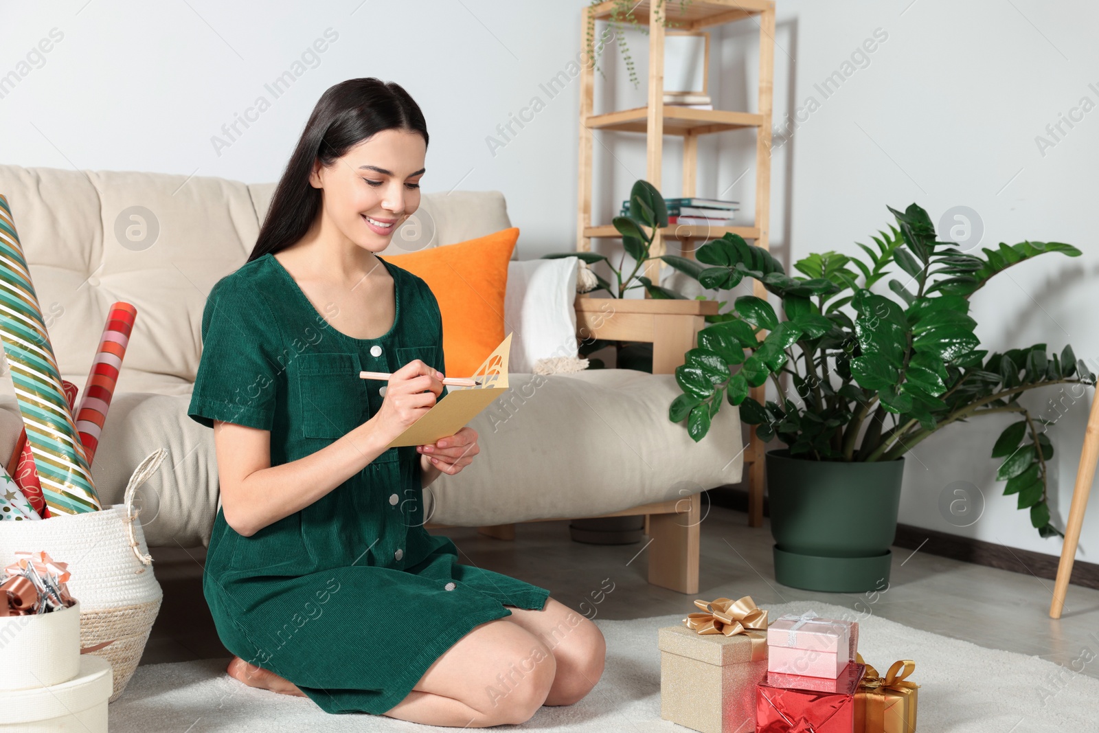 Photo of Happy woman writing message in greeting card on floor in living room