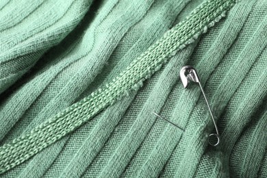 Metal safety pin on light green fabric, closeup