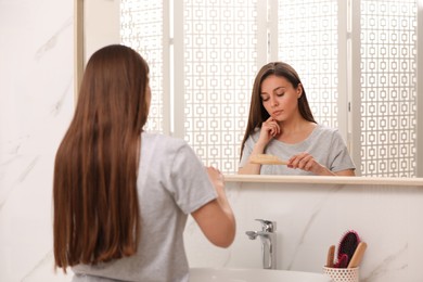 Young woman with hair loss problem near mirror in bathroom