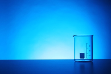 Photo of Empty beaker on table against color background. Chemistry laboratory glassware