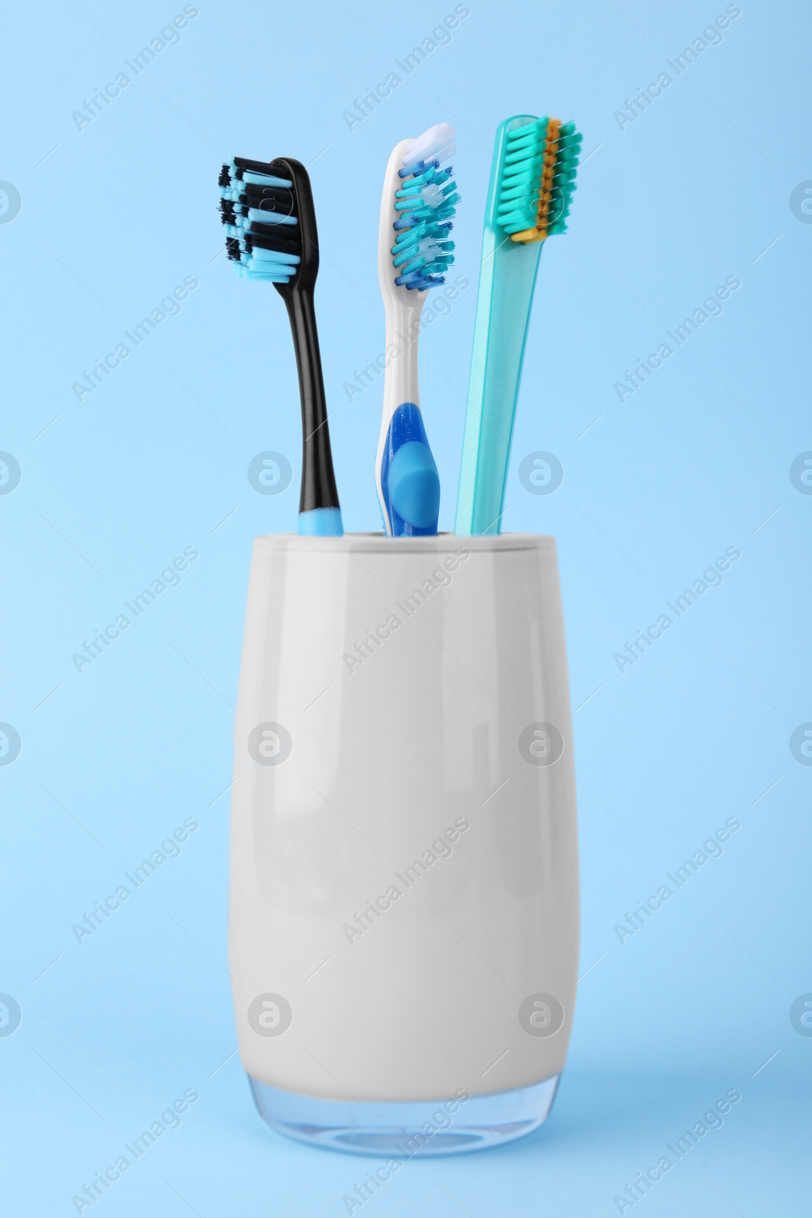 Photo of Different toothbrushes in holder on light blue background