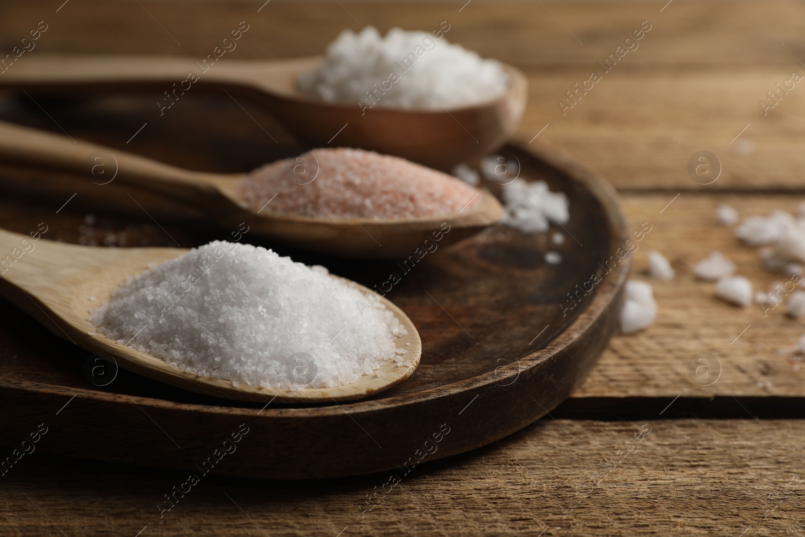 Photo of Different natural salt in spoons on wooden table, closeup. Space for text