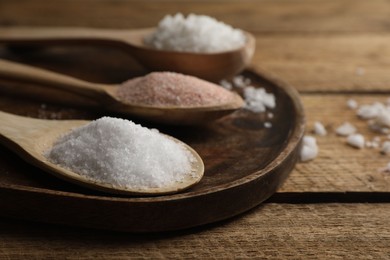 Photo of Different natural salt in spoons on wooden table, closeup. Space for text