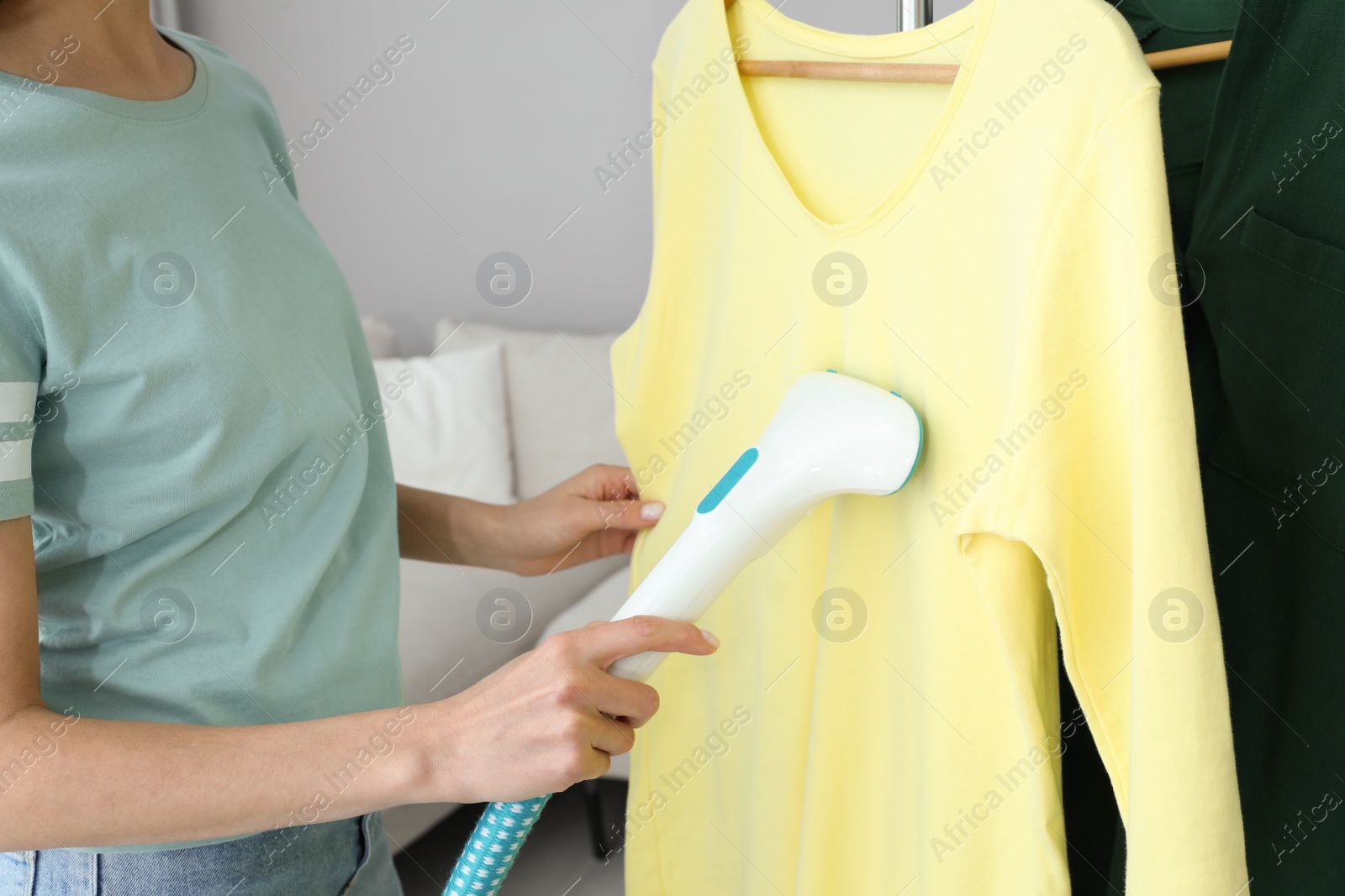Photo of Woman steaming yellow shirt at home, closeup
