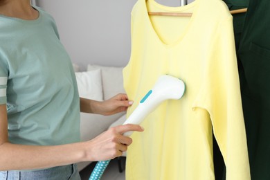 Photo of Woman steaming yellow shirt at home, closeup