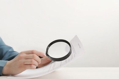 Woman looking at document through magnifier at white wooden table, closeup. Searching concept