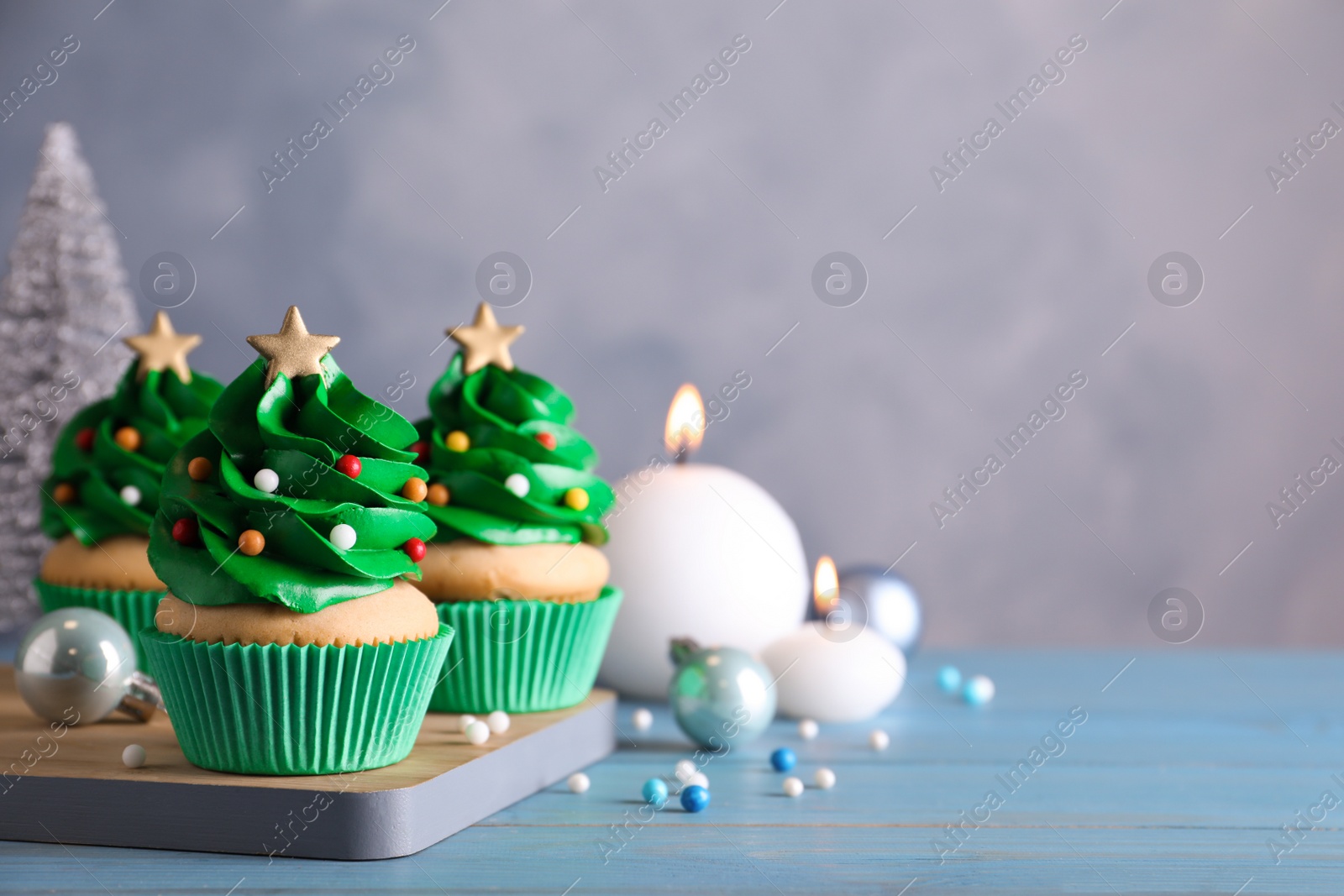 Photo of Christmas tree shaped cupcakes and decor on light blue wooden table. Space for text